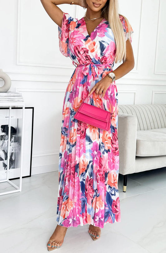Frau in langem, geblümtem Kleid mit rosa Handtasche, steht in modernem Wohnzimmer. Elegantes Sommeroutfit, modische Accessoires, stilvolle Einrichtung.