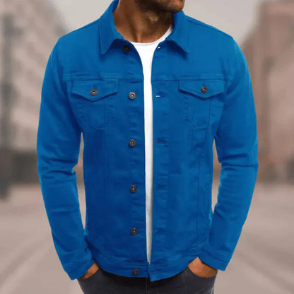 Mann trägt blaue Jeansjacke, weißes T-Shirt, Hände in Hosentaschen. Modetrend, Freizeitkleidung, urbaner Stil, Herrenmode.