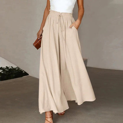 Frau in beiger, weiter Hose mit hoher Taille und weißem Top, hält eine kleine braune Tasche. Modetrend, Sommeroutfit, lässiger Stil.