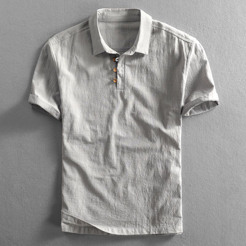 Graues Leinen-Poloshirt mit kurzen Ärmeln und Knopfleiste, auf grauem Hintergrund. Ideal für Herrenmode, Sommerkleidung, Freizeitlook.