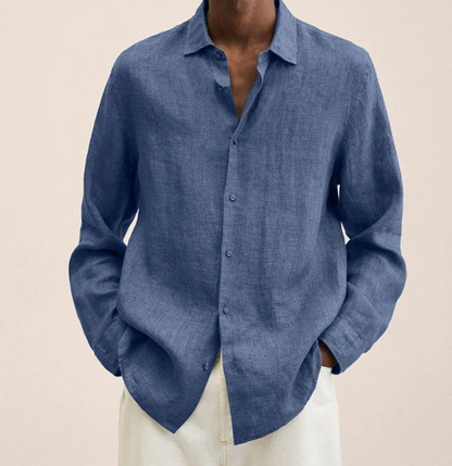 Person trägt ein blaues Leinenhemd, lässig offen, kombiniert mit weißen Hosen. Stilvolle Herrenmode, ideal für Sommer und Freizeit.