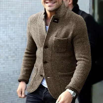 Ein Mann trägt eine braune Tweedjacke mit Knöpfen und Brusttasche, kombiniert mit einem weißen Hemd und einer schwarzen Hose. Elegante Herrenmode.
