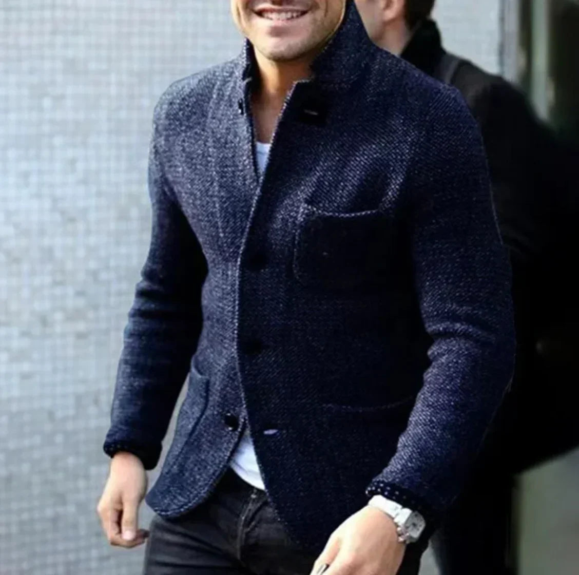 Ein Mann trägt eine stilvolle, dunkelblaue Wolljacke mit Knöpfen, kombiniert mit einem weißen Hemd und einer Armbanduhr. Elegante Herrenmode.