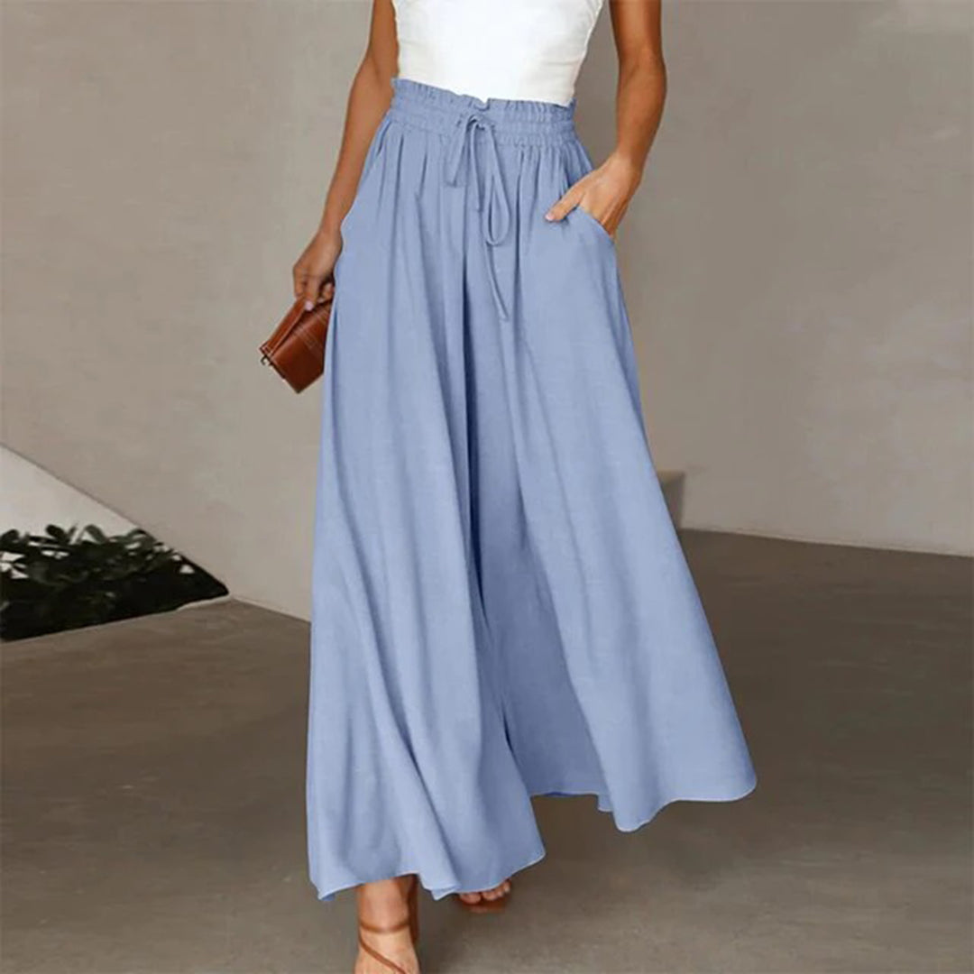 Frau in blauer, weiter Palazzo-Hose mit weißem Top, hält eine braune Clutch. Modetrend, Sommeroutfit, elegante Damenbekleidung.