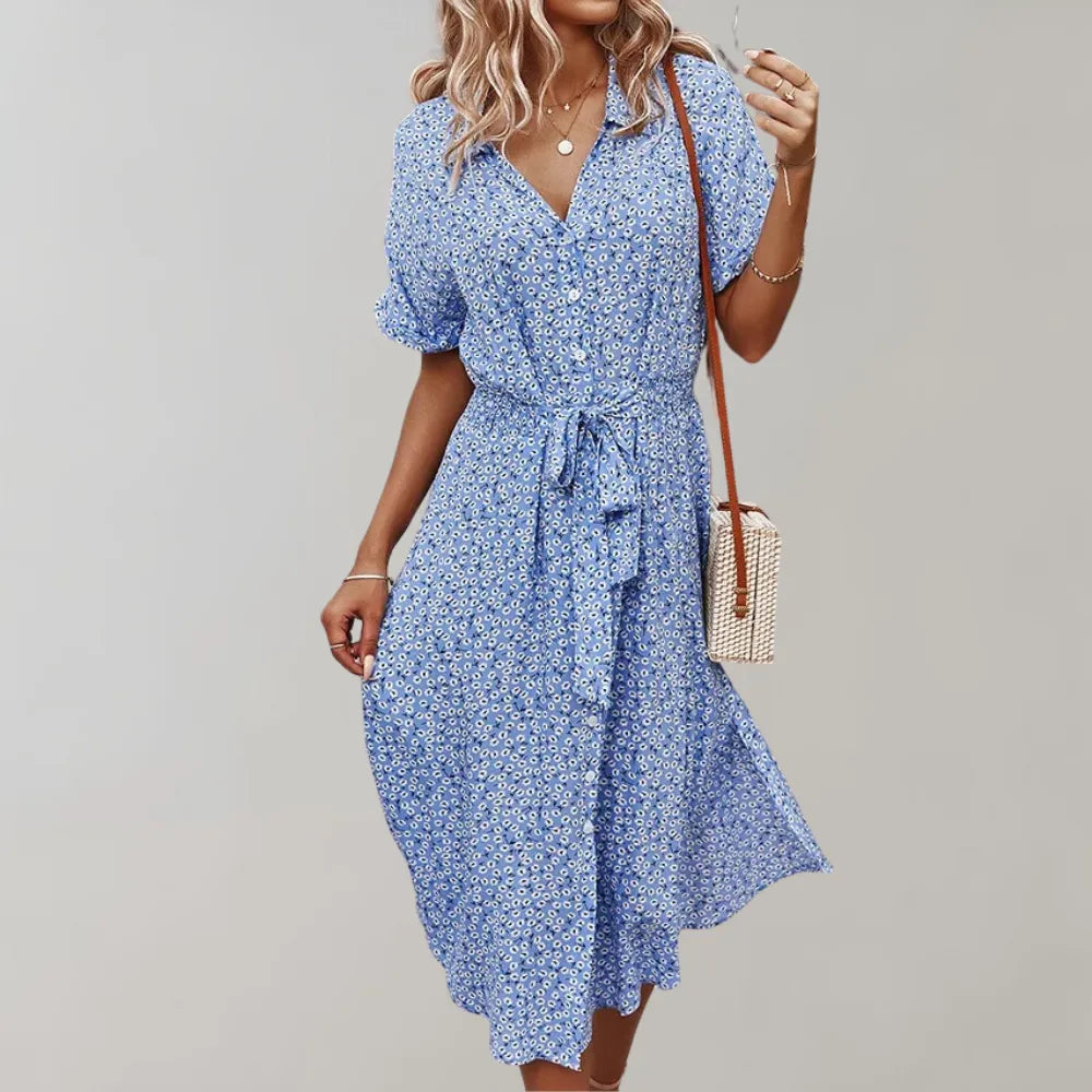 Frau in blauem Sommerkleid mit Blumenmuster, trägt eine kleine Umhängetasche. Perfekt für Freizeitmode und Sommeroutfits.
