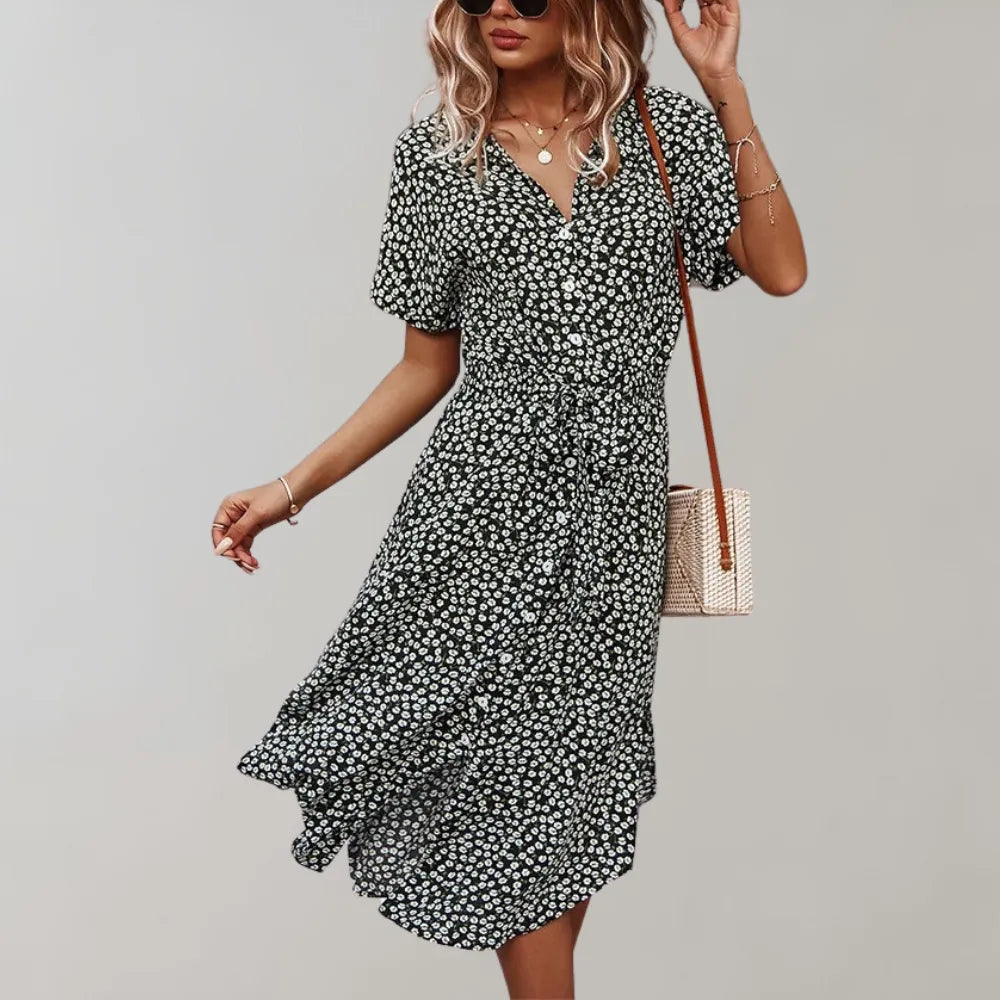 Frau in geblümtem Sommerkleid, schwarz-weiß, mit V-Ausschnitt und kurzen Ärmeln, trägt Umhängetasche. Modetrend, Damenmode, Freizeitkleidung.