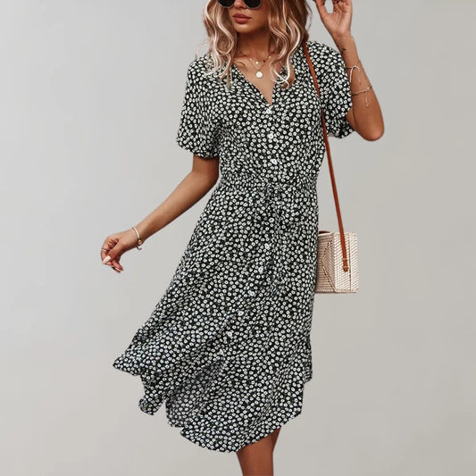 Frau in geblümtem Sommerkleid, schwarz-weiß, mit V-Ausschnitt und kurzen Ärmeln, trägt Umhängetasche. Modetrend 2023, lässiger Stil.