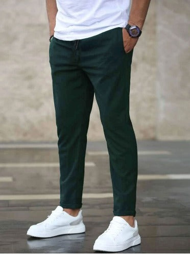 Mann in dunkelgrüner Chinohose, weißem T-Shirt und weißen Sneakers. Lässiger Herrenstil, moderne Mode, urbane Kleidung.