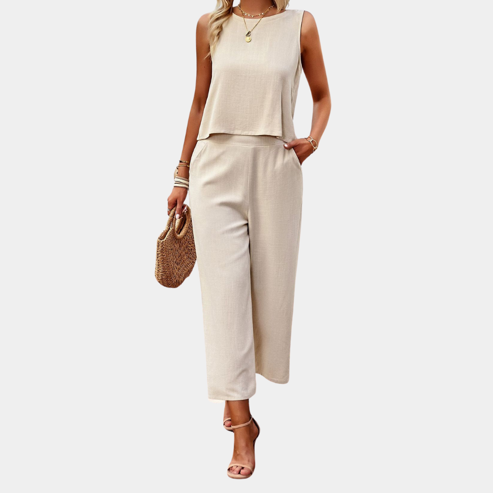 Frau in eleganter, ärmelloser, beiger Leinenhose und Top, trägt Strohtasche und Sandalen. Sommermode, Damenbekleidung, stilvoller Look.