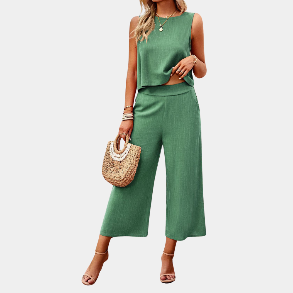 Frau in grünem Sommer-Zweiteiler mit ärmellosem Top und weiten Hosen, hält eine Strohtasche, trägt Sandalen und Schmuck. Ideal für Sommermode.