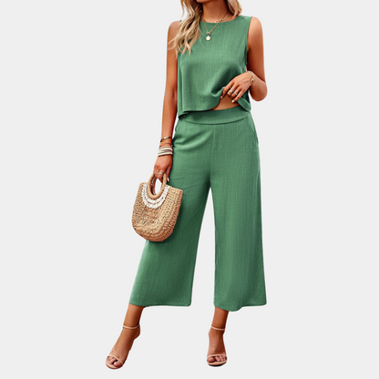 Frau in grünem Sommer-Zweiteiler mit ärmellosem Top und weiten Hosen, hält eine Strohtasche, trägt Sandalen und Schmuck. Ideal für Sommermode.