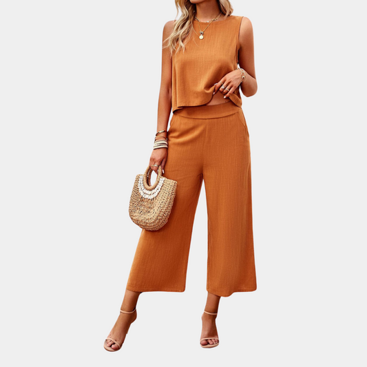 Frau in orangefarbenem, ärmellosem Jumpsuit mit weitem Bein, hält eine Strohtasche. Sommermode, eleganter Look, Damenbekleidung.