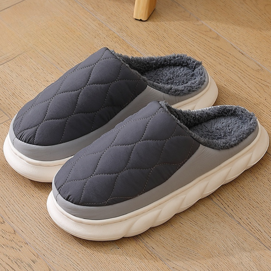Graue, gesteppte Hausschuhe mit flauschigem Innenfutter auf Holzboden. Bequeme, warme Pantoffeln für Zuhause. Ideal für kalte Wintertage.