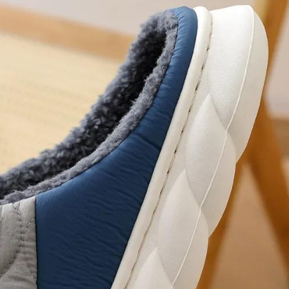 Grauer und blauer Hausschuh mit weichem Futter auf Holzstuhl. Bequeme, warme Pantoffeln für den Winter. Ideal für gemütliche Abende zu Hause.