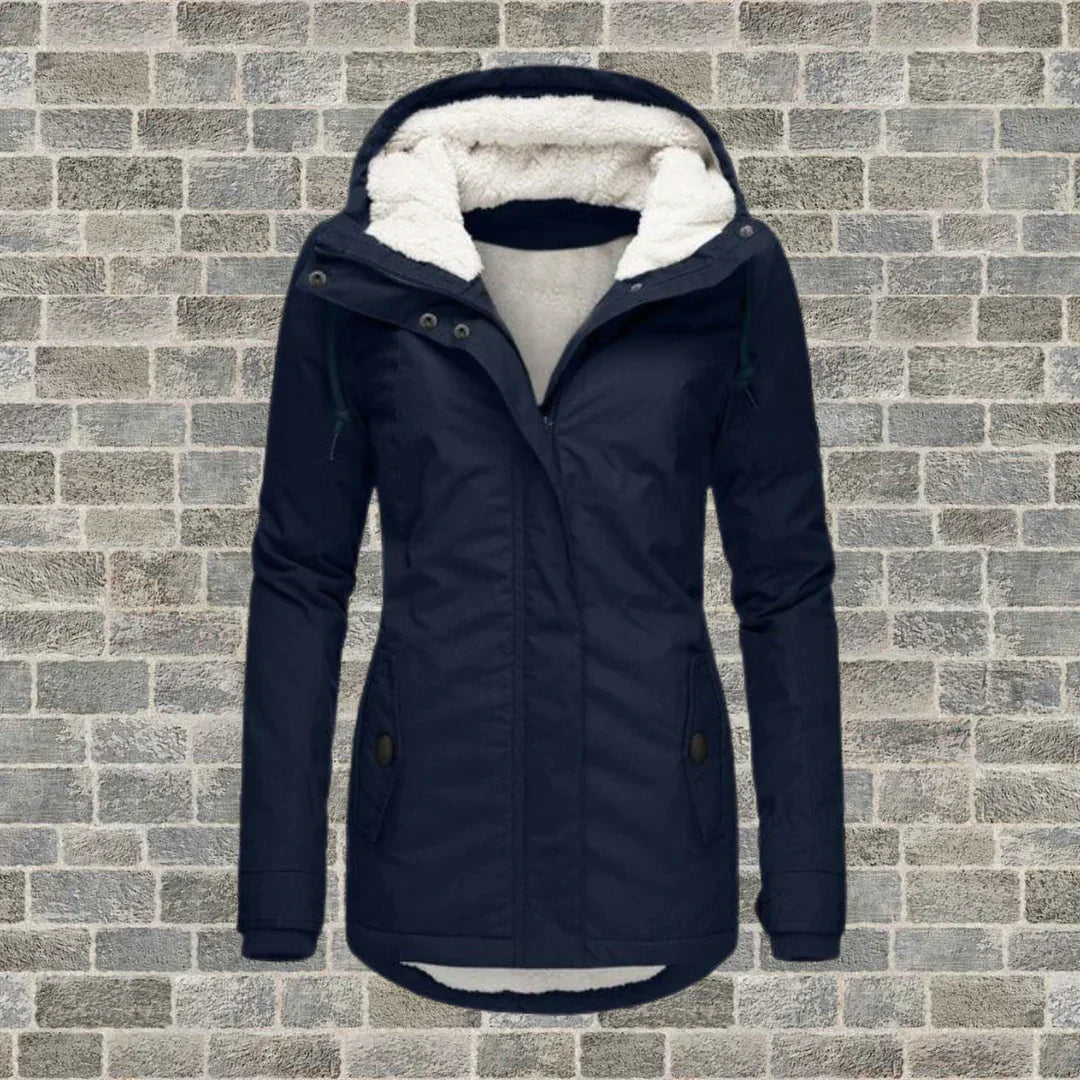 Dunkelblaue Damen-Winterjacke mit Kapuze und Fleece-Futter vor Ziegelwand. Modische, warme Outdoor-Bekleidung für kalte Tage.