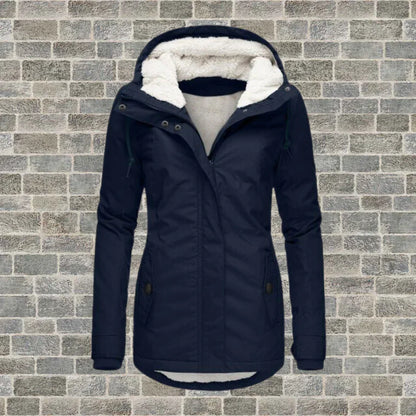 Dunkelblaue Damen-Winterjacke mit Kapuze und Fleece-Futter vor Ziegelwand. Modische, warme Outdoor-Bekleidung für kalte Tage.