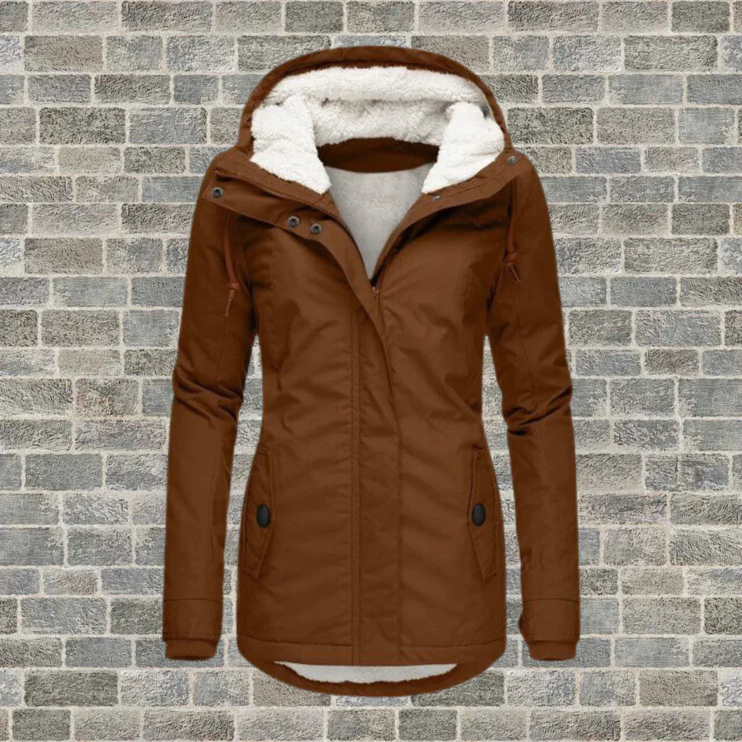 Braune Damen-Winterjacke mit Kapuze und Fleece-Futter vor Ziegelwand. Modische, warme Outdoor-Bekleidung für kalte Tage.
