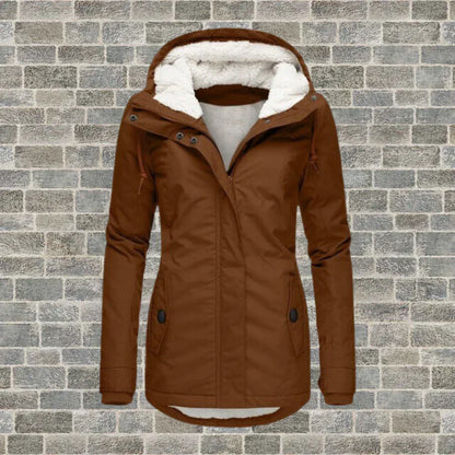 Braune Damen-Winterjacke mit Kapuze und Fleece-Futter vor Ziegelwand. Modische, warme Outdoor-Bekleidung für kalte Tage.