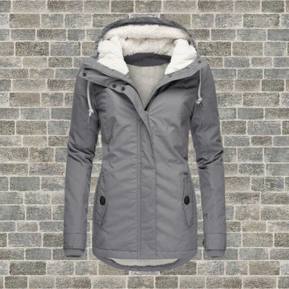 Graue Damen-Winterjacke mit Kapuze und Fleece-Futter vor Ziegelwand. Modische, warme Outdoor-Bekleidung für kalte Tage.
