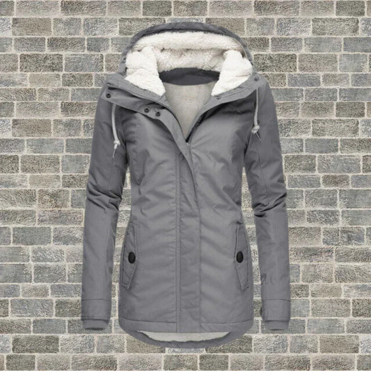 Graue Damen-Winterjacke mit Kapuze und Fleece-Futter vor Ziegelwand. Modische, warme Outdoor-Bekleidung für kalte Tage.