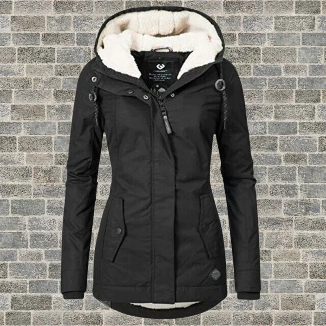 Schwarze Damen-Winterjacke mit Kapuze und weißem Futter vor Ziegelwand. Modische, warme Outdoor-Bekleidung für kalte Tage.