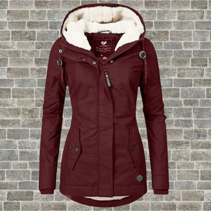 Bordeauxrote Damen-Winterjacke mit Kapuze und Fleece-Futter vor Ziegelwand. Modische, warme Outdoor-Bekleidung für kalte Tage.