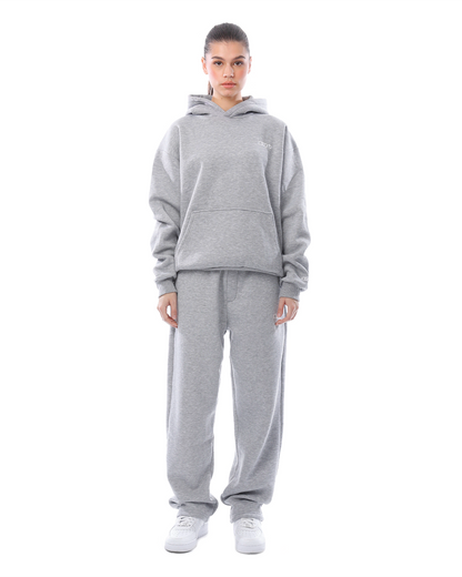 Frau in grauem Hoodie und Jogginghose, lässige Sportbekleidung, bequemer Freizeitlook, modischer Streetwear-Stil, weiße Sneaker.