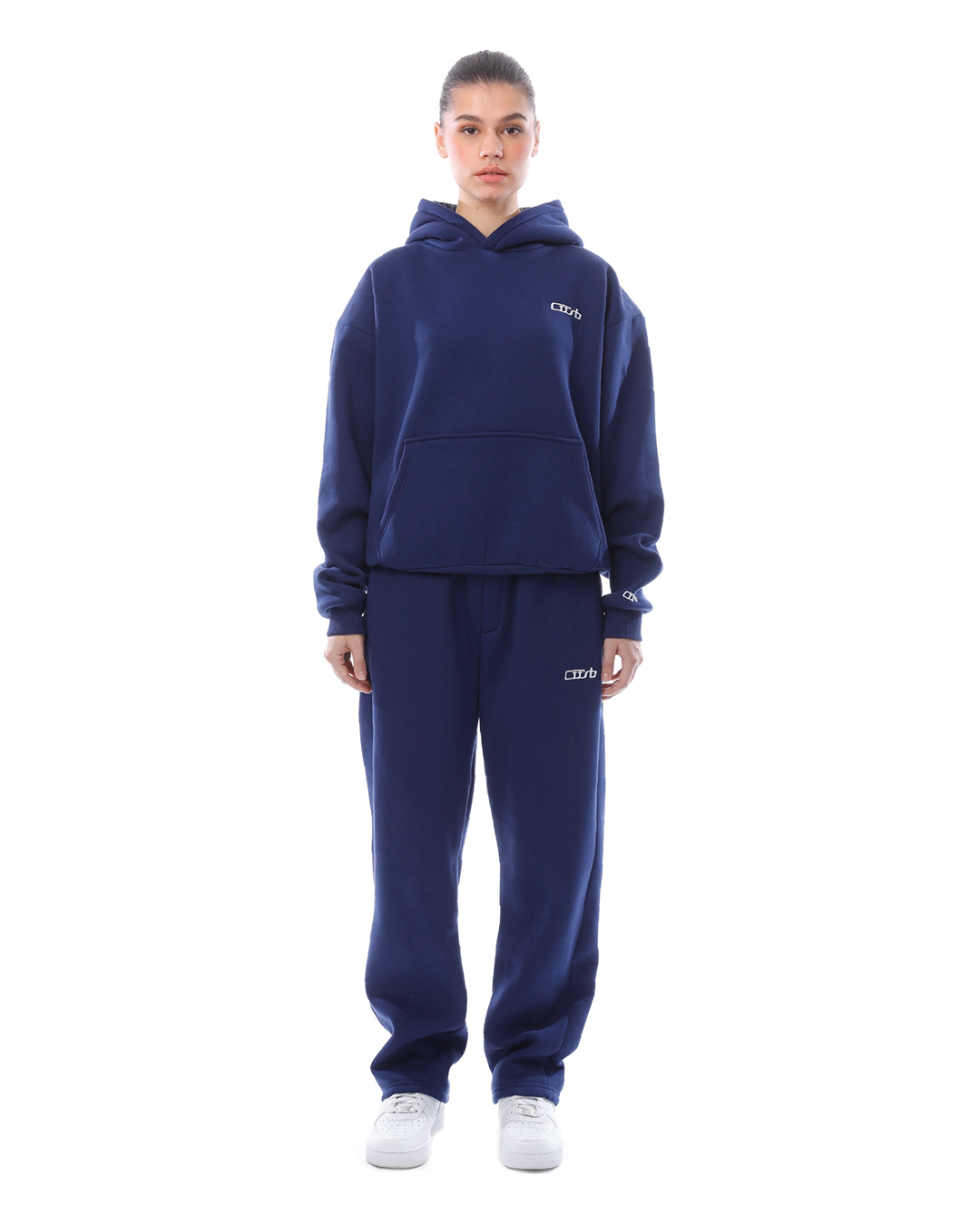 Frau in dunkelblauem Hoodie und Jogginghose, sportlicher Look, weiße Sneaker, Streetwear-Mode, bequeme Freizeitkleidung, isoliert auf weißem Hintergrund.