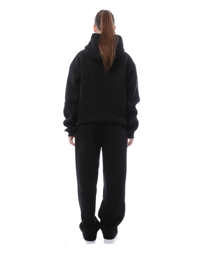 Frau in schwarzem Hoodie und Jogginghose, Rückansicht. Bequeme Freizeitkleidung, sportlicher Look, Mode für Damen, lässiger Stil.