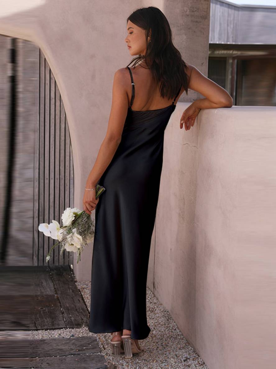 Frau in elegantem schwarzen Seidenkleid, hält Blumenstrauß, steht an moderner Architektur. Abendmode, stilvoll, luxuriös.