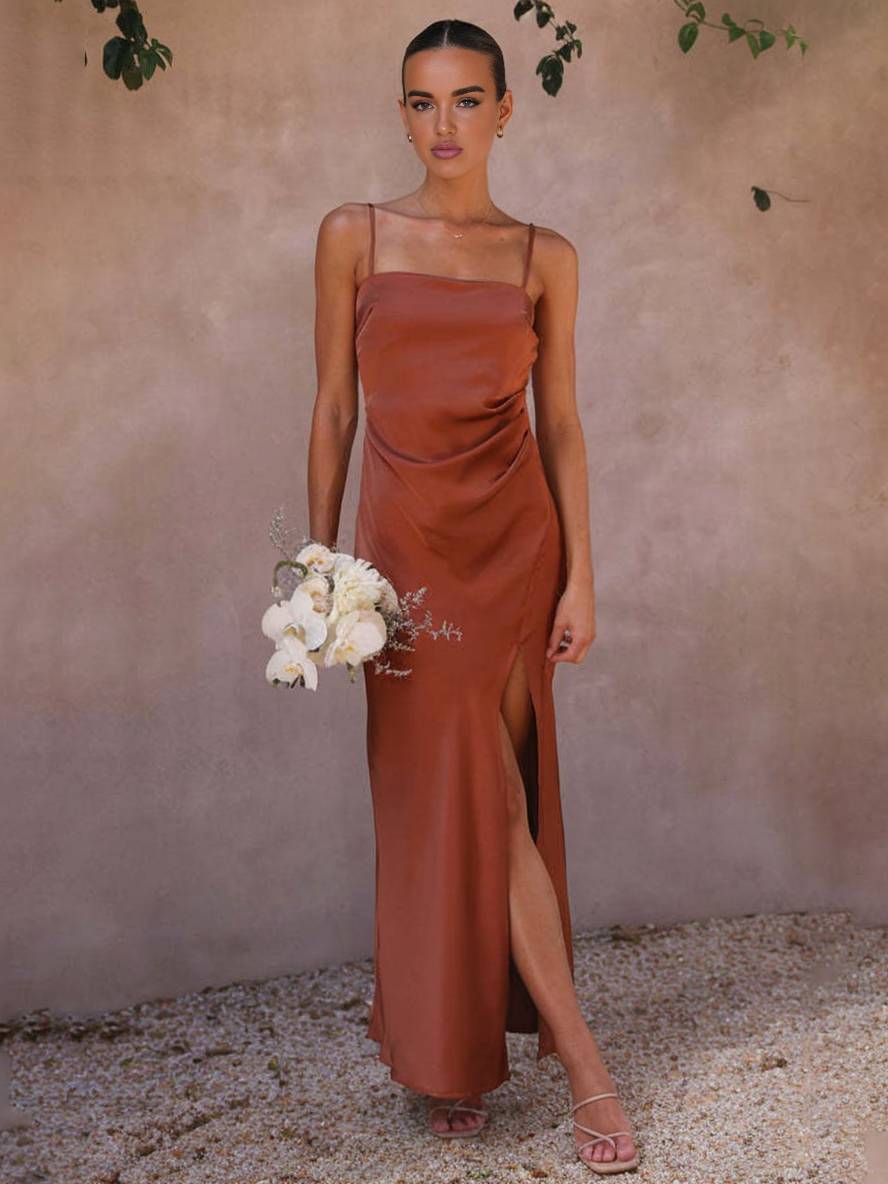 Elegantes Abendkleid in Kupfer mit Spaghettiträgern und hohem Schlitz, getragen von Frau mit Blumenstrauß. Perfekt für Hochzeiten oder formelle Anlässe.