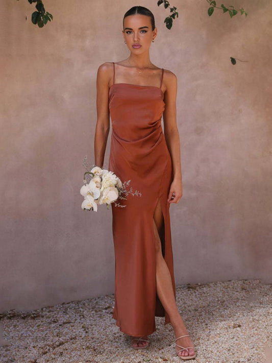 Elegantes Abendkleid in Kupfer mit Spaghettiträgern und hohem Schlitz, getragen von Frau mit Blumenstrauß. Perfekt für Hochzeiten oder formelle Anlässe.