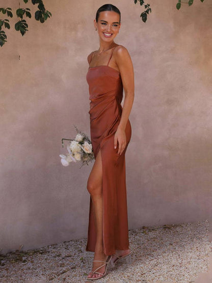 Frau in elegantem, rostfarbenem Abendkleid mit Blumenstrauß, posiert lächelnd vor beigem Hintergrund. Elegante Mode, Abendkleid, Blumenstrauß.