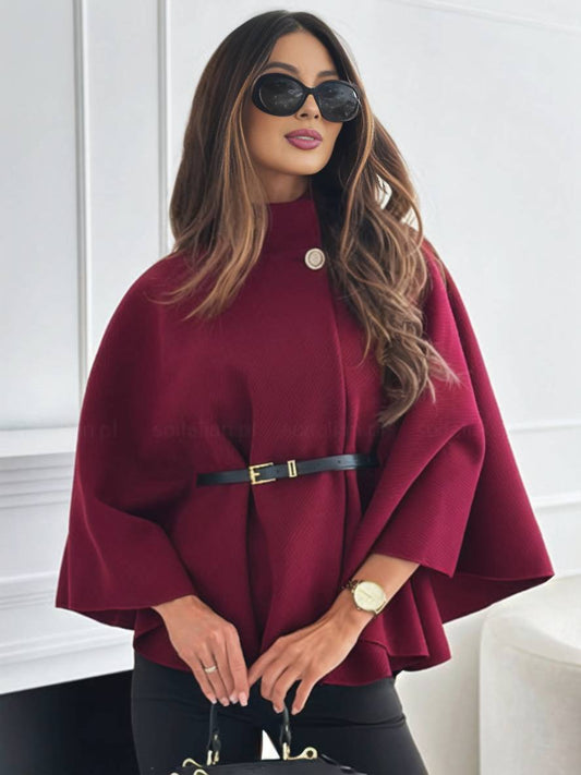 Frau in rotem Cape mit Gürtel, Sonnenbrille und langen Haaren, steht vor weißem Hintergrund. Elegante Mode, Herbstoutfit, stilvolle Kleidung.