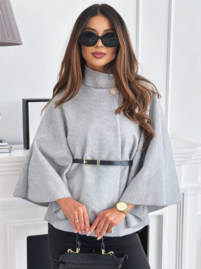 Frau mit langen Haaren trägt grauen Poncho, schwarze Sonnenbrille und Gürtel, hält schwarze Handtasche. Elegante Mode, stilvolles Outfit, Herbstlook.