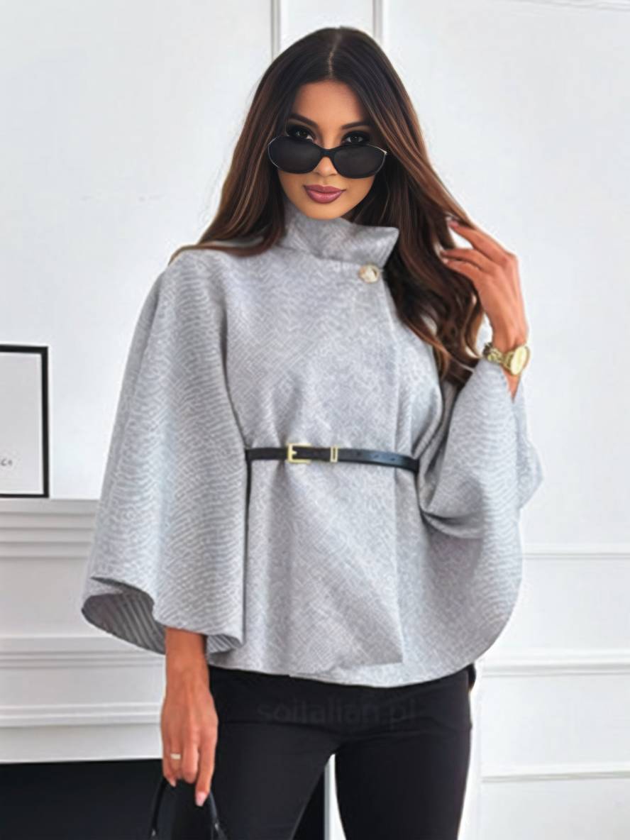 Frau in grauem Poncho mit Gürtel, Sonnenbrille und schwarzer Hose in modernem Raum. Elegante Mode, stilvolles Outfit, Herbstmode.