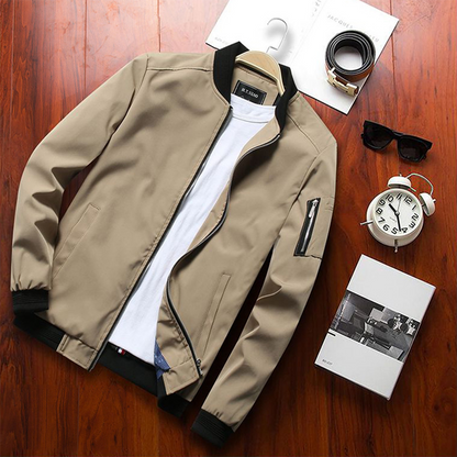 Beige Herren-Bomberjacke auf Holztisch, kombiniert mit weißem T-Shirt, Uhr, Sonnenbrille und Parfüm. Modische Herrenbekleidung Accessoires.