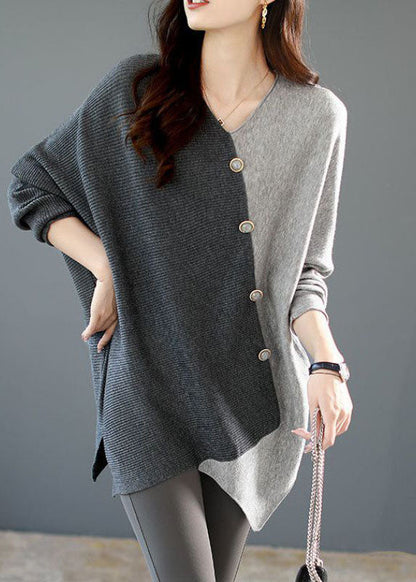 Frau trägt asymmetrischen Pullover in Grau und Schwarz mit Knopfleiste, kombiniert mit grauen Leggings. Elegante Herbstmode, Damenbekleidung.