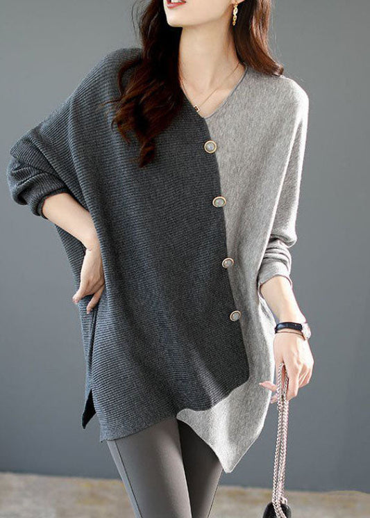 Frau trägt asymmetrischen Pullover in Grau und Schwarz mit Knopfleiste, kombiniert mit grauen Leggings. Elegante Herbstmode, Damenbekleidung.