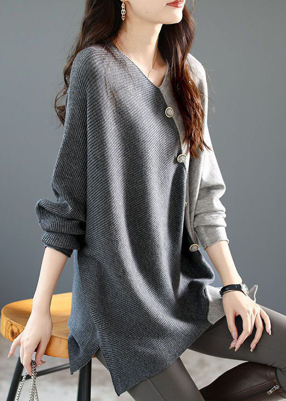 Frau trägt grauen Strickpullover mit asymmetrischem Design und Knöpfen, sitzt auf Holzstuhl. Modetrend, Damenmode, Herbstoutfit.