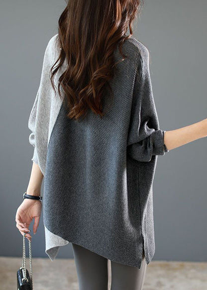 Frau in zweifarbigem Oversize-Pullover, grau und weiß, mit langen Ärmeln, hält eine kleine schwarze Handtasche. Modetrend Herbstmode Damen.