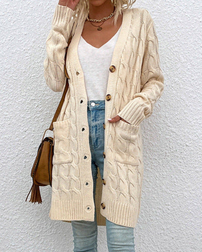 Dame in cremefarbenem Strick-Cardigan mit Zopfmuster, weißem T-Shirt und blauer Jeans vor weißer Wand. Modetrend, Herbstmode, Strickjacke.
