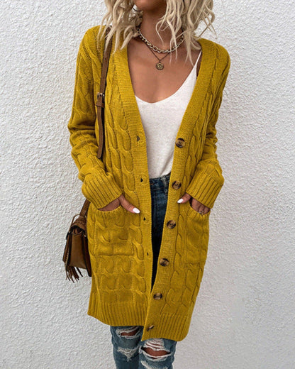 Frau in gelbem Strickcardigan mit Zopfmuster, weißem Top und zerrissenen Jeans vor weißer Wand. Modetrend, Herbstmode, lässiger Stil.
