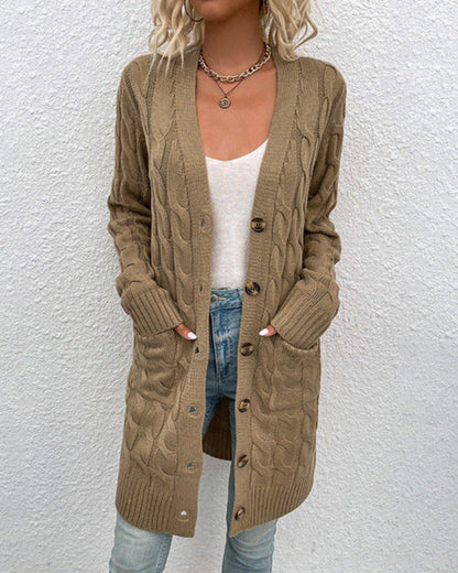 Frau trägt langen, beige Strickcardigan mit Zopfmuster, weiße Bluse und blaue Jeans. Modetrend Herbst, lässiger Look, Damenmode.
