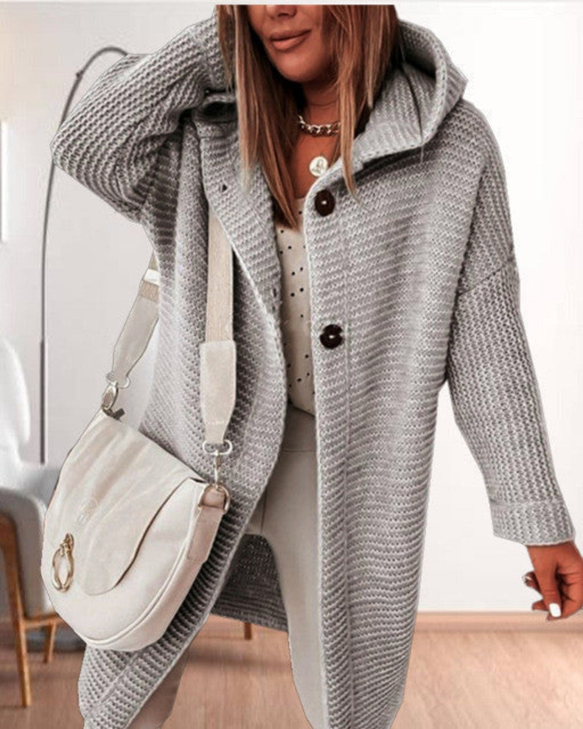 Frau in grauem Strickmantel mit Kapuze, weißer Umhängetasche und gepunkteter Bluse. Modetrend Herbst, lässiger Stil, Damenmode.