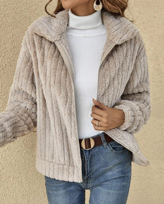 Frau in beiger Teddyfelljacke, weißem Rollkragenpullover und blauer Jeans vor beigem Hintergrund. Modetrend, Herbstmode, Damenbekleidung.