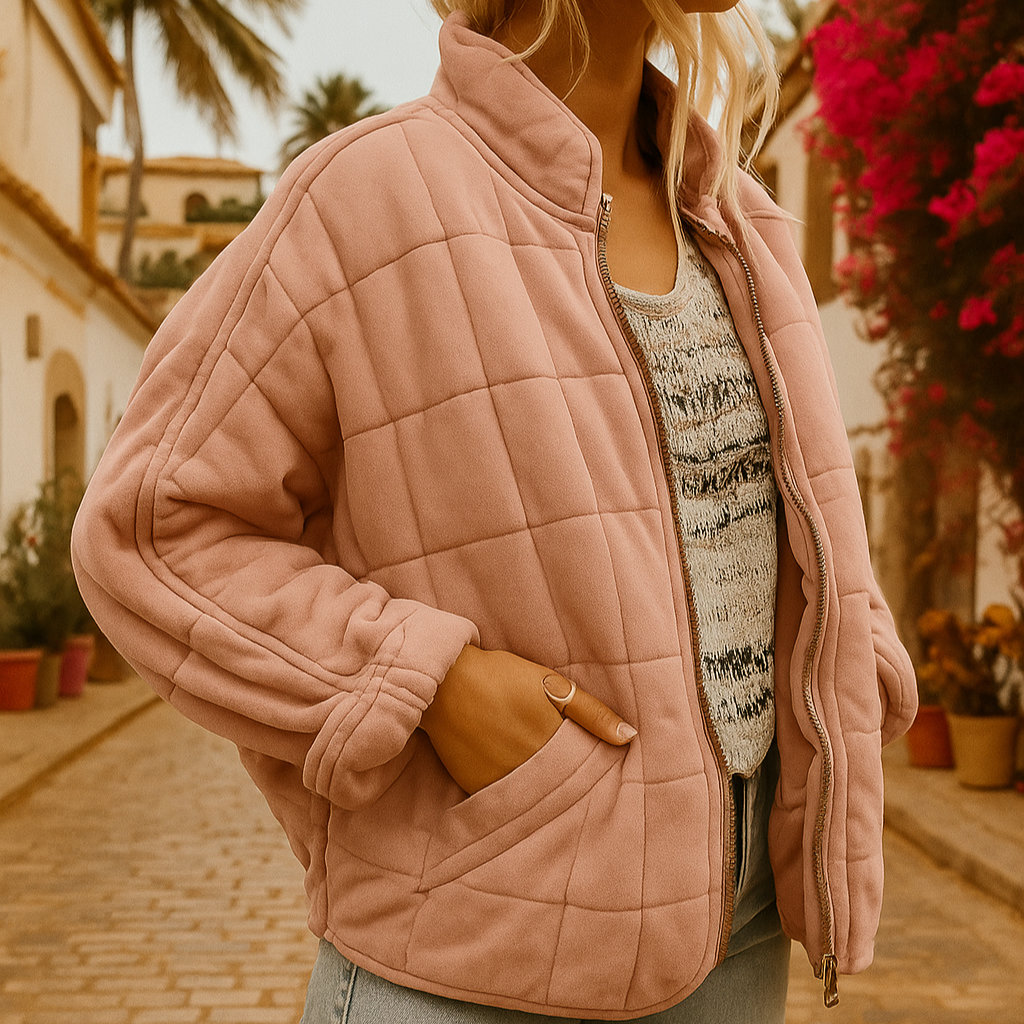 Frau in rosa Steppjacke auf gepflasterter Straße mit Palmen und blühenden Bougainvillea im Hintergrund. Modetrend, Herbstmode, Outdoor-Kleidung.
