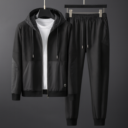 Schwarzer Trainingsanzug mit Kapuzenjacke und Jogginghose, aus atmungsaktivem Material, ideal für Sport und Freizeit, auf grauem Hintergrund.