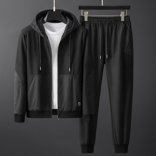 Schwarzer Trainingsanzug mit Kapuzenjacke und Jogginghose, aus atmungsaktivem Material, ideal für Sport und Freizeit, auf grauem Hintergrund.