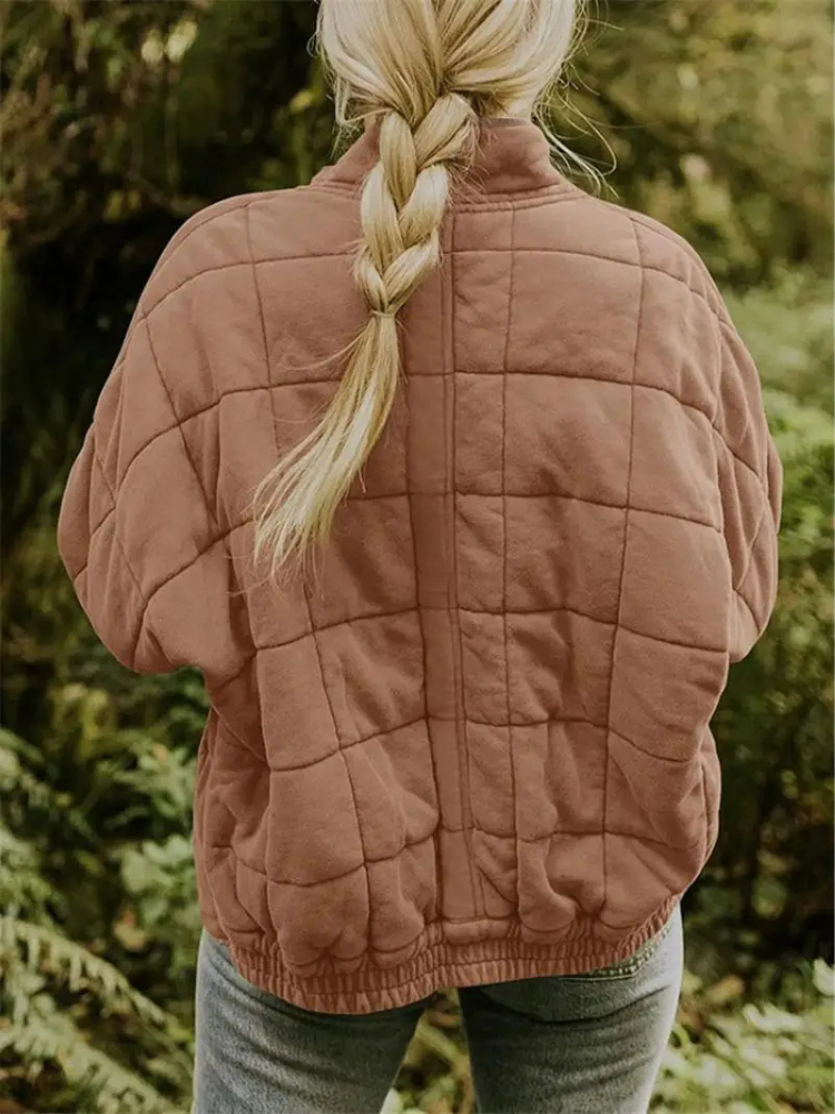 Frau mit geflochtenem Haar trägt eine gesteppte, braune Jacke im Wald. Herbstmode, Outdoor-Bekleidung, Natur, Freizeitkleidung.